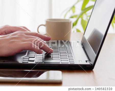 A workspace with hands operating a laptop and a cup of coffee. A workspace with hands operating a laptop and a cup of coffee. 140581310