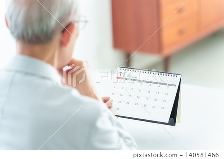 An elderly man looking at a calendar. An elderly man looking at a calendar. 140581466