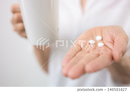 A gray-haired elderly (senior) woman taking medicine against a white background; an image representing health management, medication, medical care, and healthcare; faceless. A gray-haired elderly (senior) woman taking medicine against a white background; an image representing health management, medication, medical care, and healthcare; faceless. 140581827