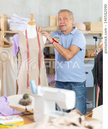 Mature man tailor connects parts of dress on mannequin 140582090