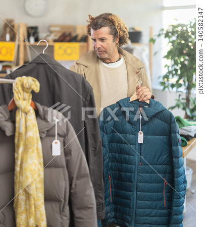 man chooses between a raincoat and a down jacket man chooses between a raincoat and a down jacket 140582147