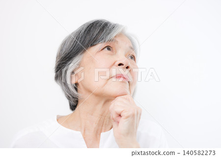 A gray-haired senior woman contemplating pensions against a white background; an image representing retirement funds, pensions, long-term care, and health anxieties. A gray-haired senior woman contemplating pensions against a white background; an image representing retirement funds, pensions, long-term care, and health anxieties. 140582273