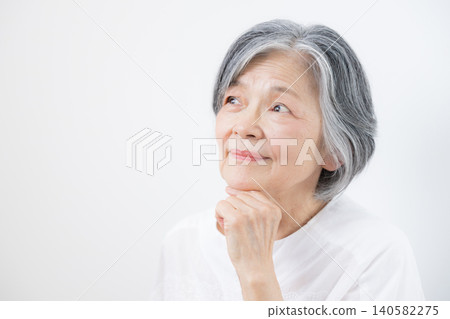 一位頭髮花白的老婦人在白色背景前思考退休金問題;這張圖片象徵著退休基金、退休金、長期照護和健康焦慮。 一位頭髮花白的老婦人在白色背景前思考退休金問題;這張圖片象徵著退休基金、退休金、長期照護和健康焦慮。 140582275