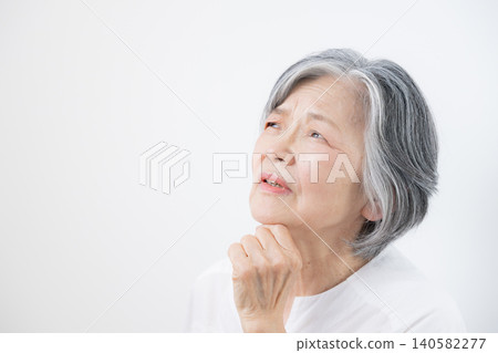 A gray-haired senior woman contemplating pensions against a white background; an image representing retirement funds, pensions, long-term care, and health anxieties. A gray-haired senior woman contemplating pensions against a white background; an image representing retirement funds, pensions, long-term care, and health anxieties. 140582277