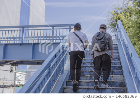 Two figures climbing the stairs of a pedestrian overpass; their faces are not visible. Two figures climbing the stairs of a pedestrian overpass; their faces are not visible. 140582369