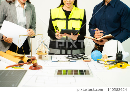 Legal and engineering professionals reviewing building plans with justice scale, gavel and safety equipment, symbolizing construction law, property regulation Legal and engineering professionals reviewing building plans with justice scale, gavel and safety equipment, symbolizing construction law, property regulation 140582624