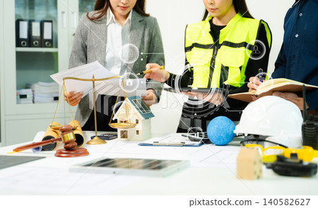 Legal and engineering professionals reviewing building plans with justice scale, gavel and safety equipment, symbolizing construction law, property regulation 140582627