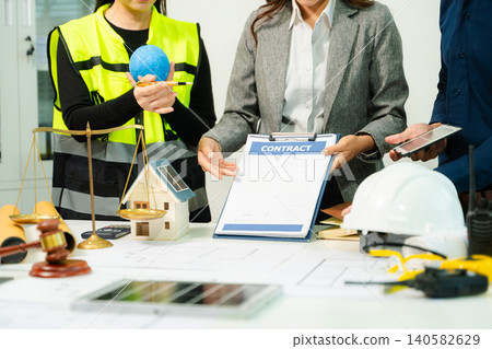 Engineers, architects and legal professionals reviewing building plans with justice scale and gavel, symbolizing construction law, property regulation, contract Engineers, architects and legal professionals reviewing building plans with justice scale and gavel, symbolizing construction law, property regulation, contract 140582629