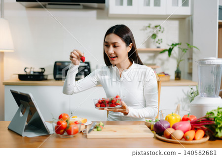 Healthy woman cooking at home while video calling online. Clean eating, nutrition, fresh vegetables, smoothie and digital lifestyle concept in modern kitchen. Healthy woman cooking at home while video calling online. Clean eating, nutrition, fresh vegetables, smoothie and digital lifestyle concept in modern kitchen. 140582681
