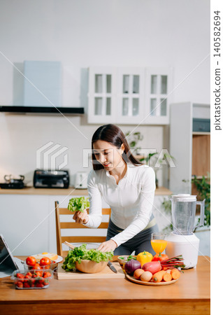 Asian woman preparing fresh salad, reflecting healthy lifestyle, clean eating, nutrition, organic vegetables, and modern home kitchen environment. 140582694