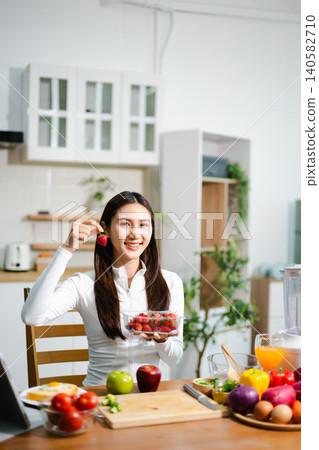 Young woman preparing fresh tomatoes and vegetables in modern kitchen. Healthy cooking, smoothie blender, clean eating, vegan lifestyle and online food blog concept. Young woman preparing fresh tomatoes and vegetables in modern kitchen. Healthy cooking, smoothie blender, clean eating, vegan lifestyle and online food blog concept. 140582710