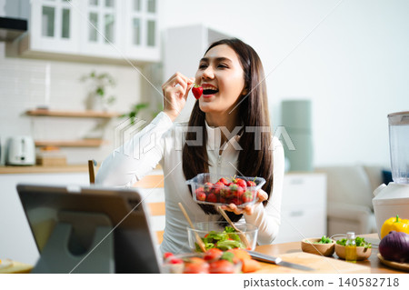 Young woman eating fresh salad in modern kitchen while using tablet. Healthy food, diet lifestyle, online cooking tutorial, wellness and clean eating concept. Young woman eating fresh salad in modern kitchen while using tablet. Healthy food, diet lifestyle, online cooking tutorial, wellness and clean eating concept. 140582718