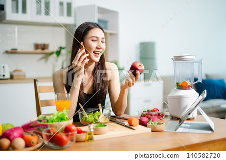 Asian fitness woman talking on phone in kitchen with orange juice 140582720