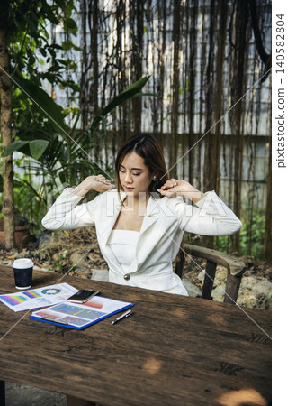 Woman streching arm raised sitting incorrect position home office desk. Back side of young asian woman tired from work body stress back pain office syndrome. Female work from home new normal concept Woman streching arm raised sitting incorrect position home office desk. Back side of young asian woman tired from work body stress back pain office syndrome. Female work from home new normal concept 140582804