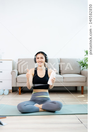 Smiling woman doing home fitness workout with tablet and headphones, showing thumbs up. Online training, healthy lifestyle, wellness and digital exercise concept. Smiling woman doing home fitness workout with tablet and headphones, showing thumbs up. Online training, healthy lifestyle, wellness and digital exercise concept. 140582850