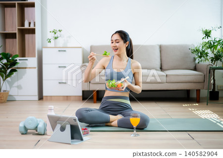 Healthy fitness woman eating fresh salad at home after workout. Clean eating, wellness lifestyle, home fitness routine, nutrition, balance and modern living concept. Healthy fitness woman eating fresh salad at home after workout. Clean eating, wellness lifestyle, home fitness routine, nutrition, balance and modern living concept. 140582904