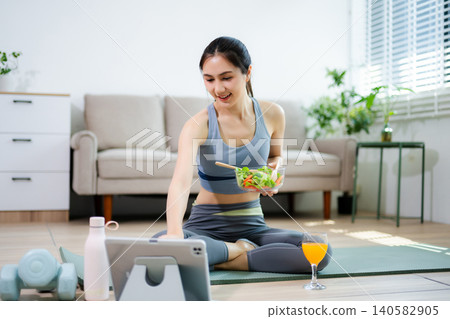 Healthy fitness woman eating fresh salad at home after workout. Clean eating, wellness lifestyle, home fitness routine, nutrition, balance and modern living concept. Healthy fitness woman eating fresh salad at home after workout. Clean eating, wellness lifestyle, home fitness routine, nutrition, balance and modern living concept. 140582905