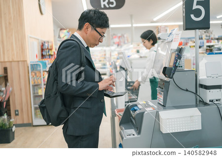 A man in a suit paying at a self-checkout counter in a supermarket. A man in a suit paying at a self-checkout counter in a supermarket. 140582948