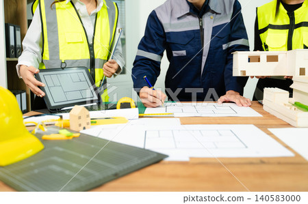 Engineers and architects reviewing digital blueprint on tablet with tools and plans on desk, representing construction planning, teamwork, engineering design Engineers and architects reviewing digital blueprint on tablet with tools and plans on desk, representing construction planning, teamwork, engineering design 140583000