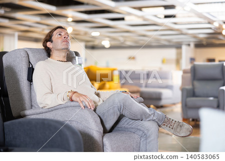 Man in a furniture store chooses an armchair Man in a furniture store chooses an armchair 140583065
