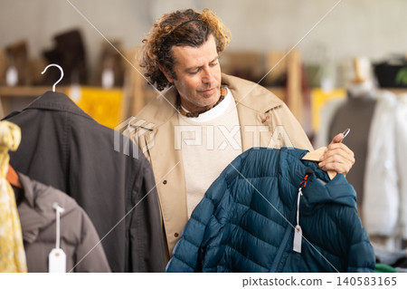 man chooses between a raincoat and a down jacket man chooses between a raincoat and a down jacket 140583165