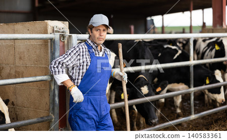 Portrait of positive male farm worker in cowshed Portrait of positive male farm worker in cowshed 140583361