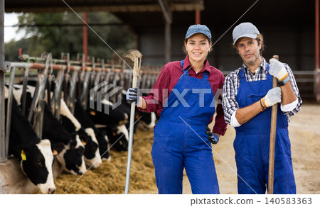 Two skilled adult young male and female farmers standing with working tools on dairy livestock farm in autumn Two skilled adult young male and female farmers standing with working tools on dairy livestock farm in autumn 140583363