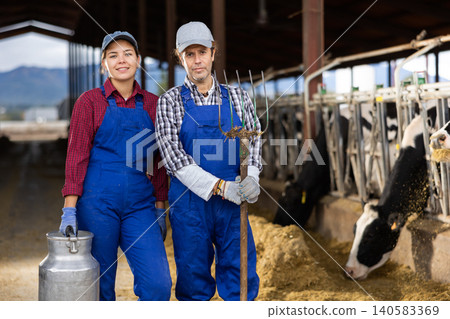 Positive diverse cow farm workers squatting in cowshed 140583369