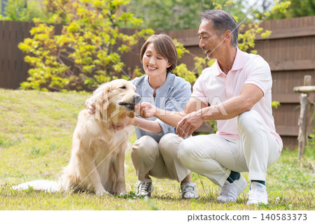 A smiling senior couple enjoying time with their golden retriever in the garden. A smiling senior couple enjoying time with their golden retriever in the garden. 140583373