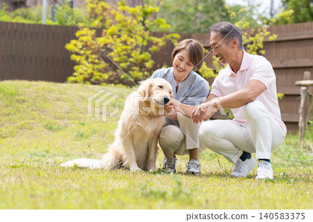 一對面帶笑容的老夫婦在花園裡和他們的金毛犬享受美好時光。 一對面帶笑容的老夫婦在花園裡和他們的金毛犬享受美好時光。 140583375