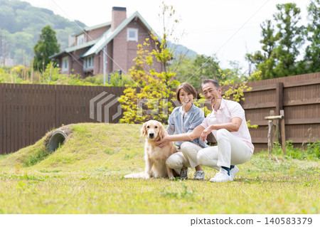 一對面帶笑容的老夫婦在花園裡和他們的金毛犬享受美好時光。 一對面帶笑容的老夫婦在花園裡和他們的金毛犬享受美好時光。 140583379