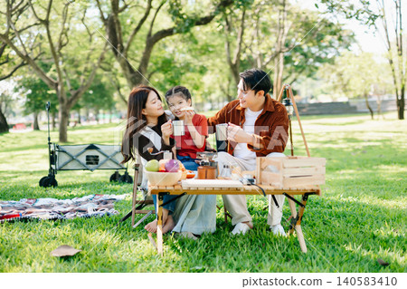 Joyful family enjoying a sunny picnic with music and laughter. Parents and child bonding outdoors, surrounded by love Joyful family enjoying a sunny picnic with music and laughter. Parents and child bonding outdoors, surrounded by love 140583410
