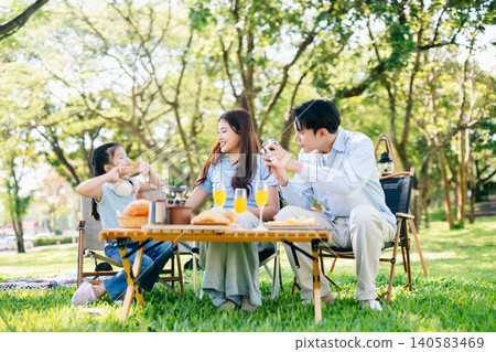 Joyful family picnic moment as daughter takes photo of smiling parents raising orange juice in a sunny park. A warm, happy lifestyle full Joyful family picnic moment as daughter takes photo of smiling parents raising orange juice in a sunny park. A warm, happy lifestyle full 140583469
