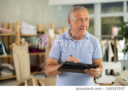 Mature man drawing on tablet in sewing salon Mature man drawing on tablet in sewing salon 140583507
