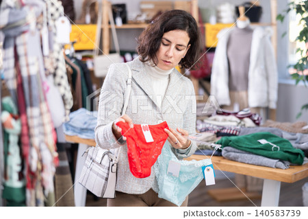 Focused woman viewing underwear and shopping red panties in lingerie store Focused woman viewing underwear and shopping red panties in lingerie store 140583739