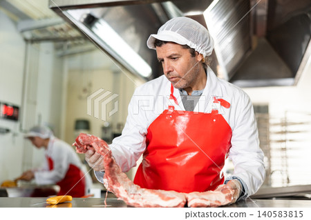 Butchery worker preparing slab of raw pork ribs for packaging 140583815