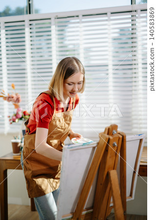 A female artist painting on canvas in a bright home studio, expressing creativity and focus. A female artist painting on canvas in a bright home studio, expressing creativity and focus. 140583869