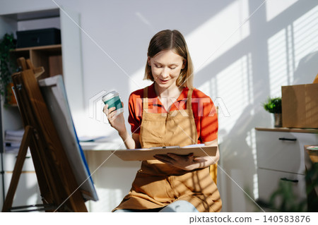 A focused female artist holding her coffee while sketching ideas in her sunlit studio, capturing creativity, peaceful workflow, and an inspiring artistic routine. A focused female artist holding her coffee while sketching ideas in her sunlit studio, capturing creativity, peaceful workflow, and an inspiring artistic routine. 140583876