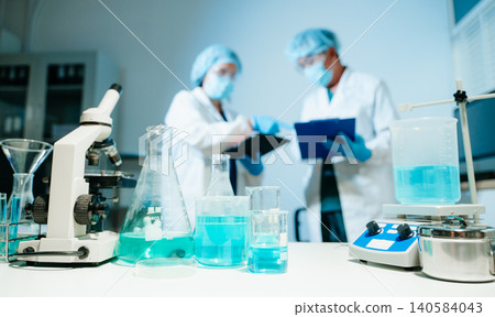 Scientists collaborating in medical laboratory with microscope and glassware for pharmaceutical research, chemistry testing, healthcare innovation and clinical development. Scientists collaborating in medical laboratory with microscope and glassware for pharmaceutical research, chemistry testing, healthcare innovation and clinical development. 140584043