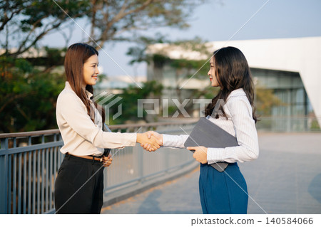 Asian businesswomen celebrating success with a handshake, symbolizing partnership, teamwork, and business deal achievement in corporate environment. Asian businesswomen celebrating success with a handshake, symbolizing partnership, teamwork, and business deal achievement in corporate environment. 140584066