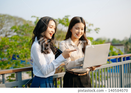 Asian businesswomen discussing strategy outdoors, reviewing documents and planning projects. Modern teamwork, collaboration, and professional corporate Asian businesswomen discussing strategy outdoors, reviewing documents and planning projects. Modern teamwork, collaboration, and professional corporate 140584070