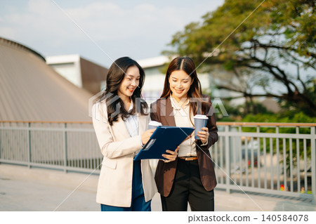 Asian businesswomen discussing strategy outdoors, reviewing documents and planning projects. Modern teamwork, collaboration, and professional corporate Asian businesswomen discussing strategy outdoors, reviewing documents and planning projects. Modern teamwork, collaboration, and professional corporate 140584078