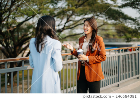 Two Asian businesswomen collaborating with digital tablet outdoors in modern corporate setting. Teamwork, technology, leadership Two Asian businesswomen collaborating with digital tablet outdoors in modern corporate setting. Teamwork, technology, leadership 140584081