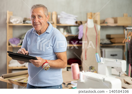 Mature man drawing on tablet in sewing salon 140584106