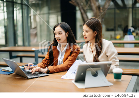 Asian businesswomen collaborating outdoors using laptop and tablet, discussing strategy and planning. Modern teamwork, digital workflow Asian businesswomen collaborating outdoors using laptop and tablet, discussing strategy and planning. Modern teamwork, digital workflow 140584122