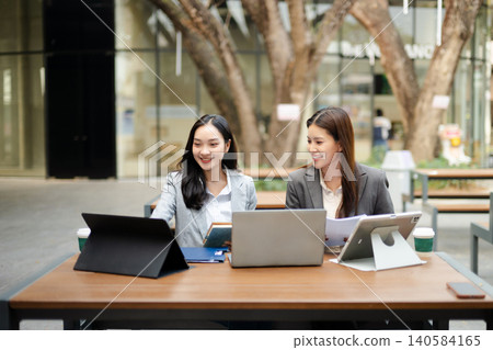 Businesswomen collaborating with laptop and tablet in a modern workspace, representing teamwork, communication, startup planning, leadership and corporate strategy. Businesswomen collaborating with laptop and tablet in a modern workspace, representing teamwork, communication, startup planning, leadership and corporate strategy. 140584165