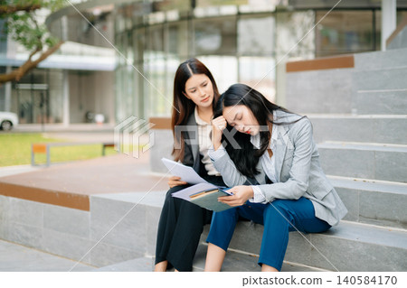 Businesswoman feeling stressed while reviewing documents as supportive colleague comforts her, representing workplace pressure, teamwork Businesswoman feeling stressed while reviewing documents as supportive colleague comforts her, representing workplace pressure, teamwork 140584170