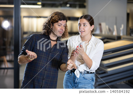 Married couple is actively discussing and comparing prices in a smartphone with prices on price tags in hardware and plumbing store 140584192