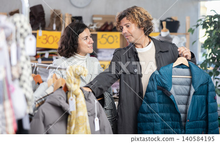 man chooses a jacket in a store with a woman man chooses a jacket in a store with a woman 140584195