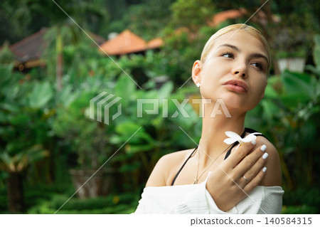 Young woman poses with a flower in a lush garden 140584315